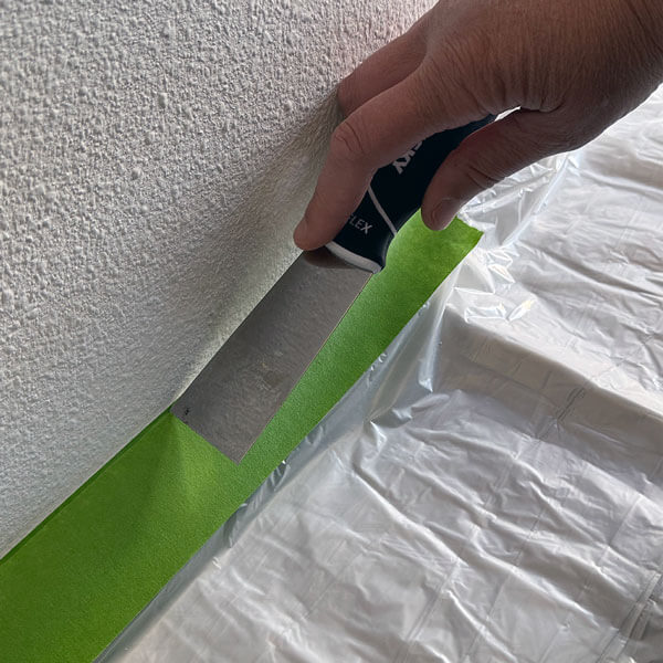 Applying painter's tape to the baseboard and pressing it down with a putty knife