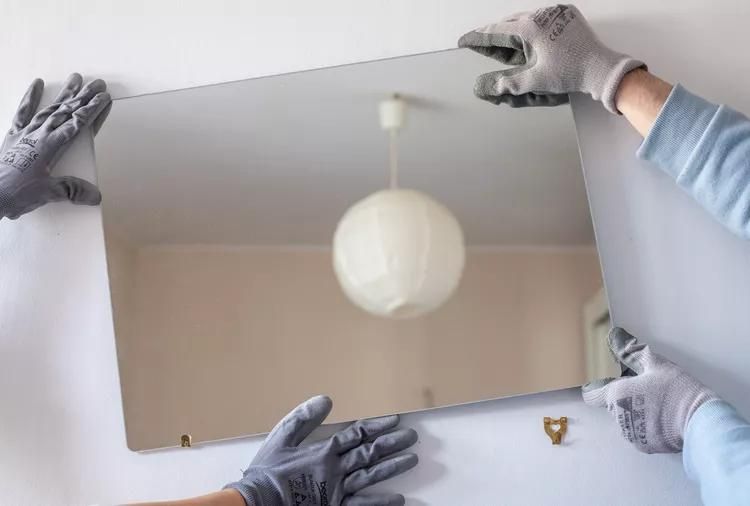 carefully pulling the mirror off the wall with two hands